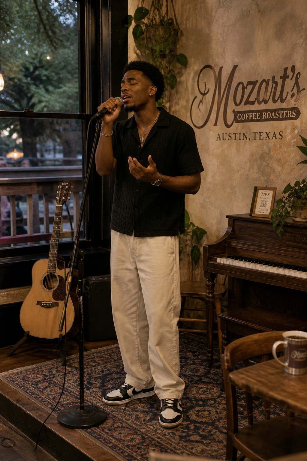 Singer on a small coffeehouse stage in a black camp-collar shirt